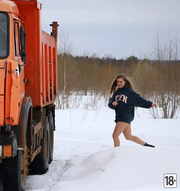 Молодая обнаженная красотка в снегу у оранжевого КамАЗа